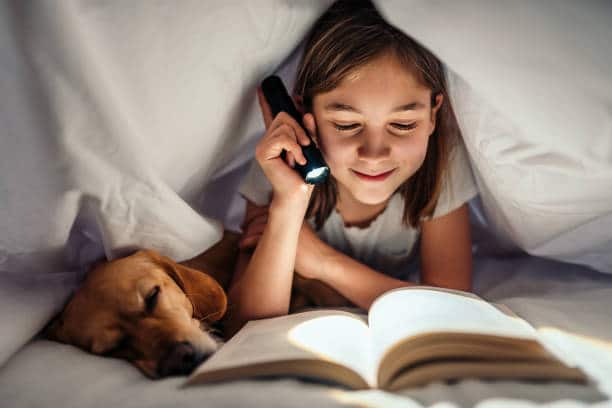 Petite fille lisant un roman pour enfant en cachette sous la couette.