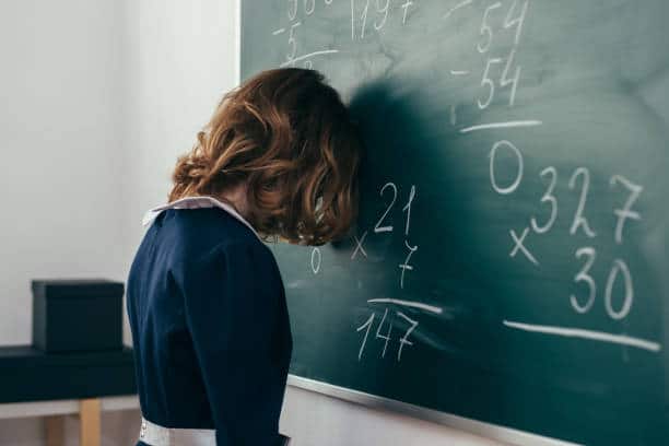 Un enfant se désespère devant un tableau noir couvert de signes d’algèbre. 